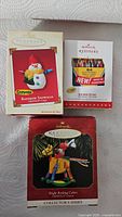 Photo showing three Hallmark Keepsake Crayola ornaments in original boxes and a sealed box of Crayola crayons, featuring the Rainbow Snowman and Bright Rocking Colors ornaments prominently.