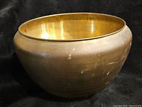 Side view of a large vintage brass bowl showing its rounded, polished body with some surface marks and patina.