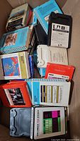 Photo showing a box filled with assorted 8 track tapes with visible labels and brands.