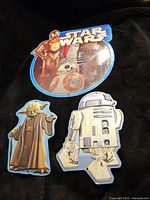 Front view of four Star Wars tin signs featuring C-3PO, BB-8, R2-D2, and Yoda characters on a dark background.
