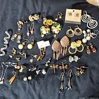 Full view of entire lot of assorted vintage and modern costume earrings laid out on black surface.