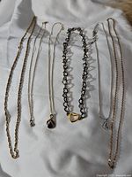Top view of seven assorted necklaces including gold-tone chains, a dark metal chain with heart pendant, and silver-tone chain with a round pendant.