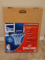 Front view of the closed original packaging showing Spalding Standard Championship Series branding, image of the rim with net, and product features.