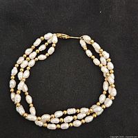 Full view of the three-strand pearl and gold bead bracelet with clasp closed.