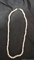 Full view of vintage pearl necklace laid out on black fabric, showing the entire length and clasp.