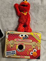 Elmo plush toy standing on original box with all labels visible