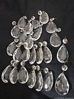 Lot of 24 clear vintage glass teardrop prisms with octagonal top connectors, laid out on black fabric background for visibility.