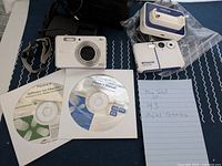Lot contents showing Fujifilm camera, software CDs, Polaroid camera, charger/dock and handwritten note listing items