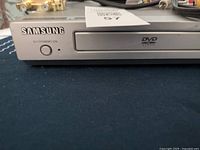 Front view of the silver Samsung DVD player showing the power button, Samsung logo, and DVD tray.