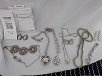 Full view of jewelry laid out including necklaces, bracelet, and earrings on white fabric background.