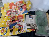 Raggedy Ann and Andy bed sheet and pillowcase laid out with the Jolly Green Giant stuffed toy in original plastic bag and a collector magazine.