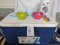 Blue and white Coleman chest cooler with three colorful bowls and spoons on top, showing overall lot contents.