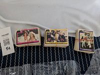 Three stacks of vintage Charlie's Angels original series trading cards shown on a cloth. Each stack has cards with different colored borders. Cards show some aging and wear.
