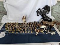 Wide view of most Red Rose Tea collectible figurines laid out with animal and horse ornaments on display over blue cloth