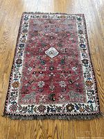Full view of the antique Hamidan style rug showcasing red field, white border with floral motifs and fringe ends.