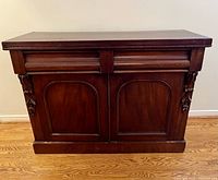 Front view of antique mahogany sideboard showing upper drawers and two lower doors with carved decoration, set on hardwood floor.