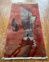 Full view of rectangular vintage wool rug with rust background showing Chinese sailboats, building, and birds in stylized Art Deco design.