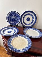 Overview of all five blue and white china plates displayed on wooden surface, including Shakespeare plate and various floral designs.