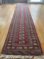 Full view of runner laid flat on wood floor showing red field and repeating medallion pattern.