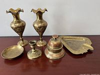Full view of all brass items together on a flat surface including the two vases, ashtray, candle holder, incense burner, and brass tray.