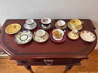 Full view of 7 sets of cups and saucers arranged on a wooden table showing variety of patterns and colors