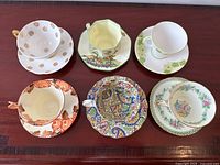 Top view of all six bone china teacups and their matching saucers arranged on a table showing varied floral and ornate patterns.