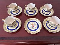 Overview of 5 demitasse cups and 7 saucers laid out on a wooden surface, showing pattern and quantity.