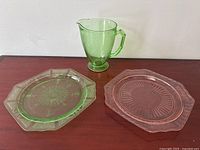 Green 7 inch glass jug with handle, and both glass plates positioned in background against a plain white wall.