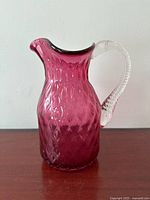 Front view of cranberry glass pitcher showing quilted pattern and clear handle