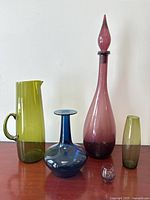Group shot of all five colored glass pieces on red surface against white wall