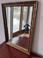 Full view of gilt-framed rectangular mirror propped against a window, showing reflective surface and frame shape.