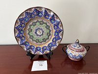Photo showing both the decorative fluted plate and the sugar bowl with lid side by side on black stands.