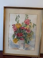 Full view of the framed watercolor painting showing floral composition of zinnias and hollyhocks in a gold frame with cream matting.