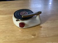 Side angle view of the Bakelite phonograph lighter showing overall shape, red knob, and metal tonearm lever on black 'record'.