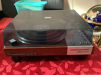 Front view of closed turntable showing wood-grain plinth, brushed aluminum faceplate with controls and transparent dust cover