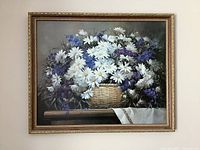 Frontal view of large framed floral print showing a basket of daisies and purple flowers, with a gold ornate frame and treated glass.