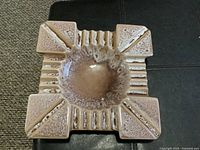 Overhead view of the large square ceramic ashtray showing the central recessed bowl with mottled brown glaze and four raised corner rests with vertical ridges in between.