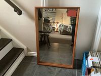 Full view of the large rectangular mirror showing its teak wood frame in natural finish placed on floor leaning against wall.