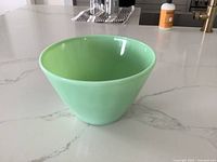 Large pale green jadeite Fire-King mixing bowl placed on white marble countertop, showing side and inside views.