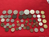 Overview photo showing the array of foreign coins arranged on a red surface to capture all items included in the lot.