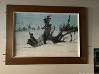 Framed oil painting showing driftwood on snow with trees in background, signed and with wooden frame