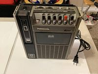 Front view of a vintage Panasonic cassette tape recorder with built-in speaker and power cord.
