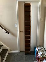 Full front view of tall pine CD shelf tower placed against wall near staircase and door.