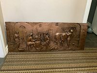 Full view of the large horizontal copper plaque resting against a wall. Shows the overall scene including men around a barrel and a horse on the right side.