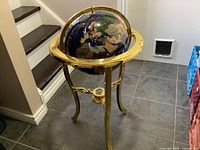 Full view of semi-precious stone globe on three-legged brass stand with compass at center.