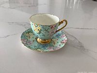 Photo of Shelley Melody cup and saucer set showing floral pattern and gold trim on a white marble surface.