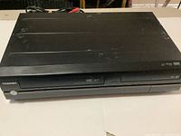 Front view of Toshiba VR7 VHS VCR DVD recorder showing black plastic housing, VHS compartment and front panel details.