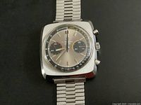 Close-up of watch face showing silver dial, black 30-minute and 60-second subdials, red central hand and tachymeter scale.