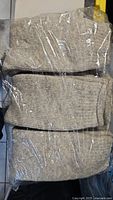 Three pairs of medium beige wool socks in plastic packaging shown from above.