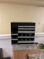 Front view of black cosmetic holder display with multiple compartments arranged in rows and rhinestone trim on each row.
